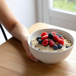 A serene and calming morning scene. A person, with a peaceful and content expression, is seated at a minimalist kitchen table, engaging in mindful eating. Their breakfast consists of a vibrant bowl of overnight oats topped with fresh berries and seeds, alongside a glass of natural yogurt or kefir. Soft, natural light illuminates the scene, highlighting the connection between nutritious food, gut health, and mental clarity, conveying a sense of self-care and a positive start to the day.